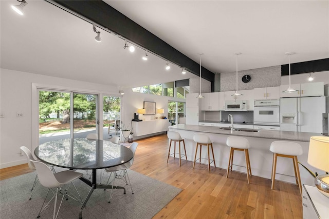 dining space with rail lighting, beamed ceiling, healthy amount of natural light, light wood finished floors, and high vaulted ceiling