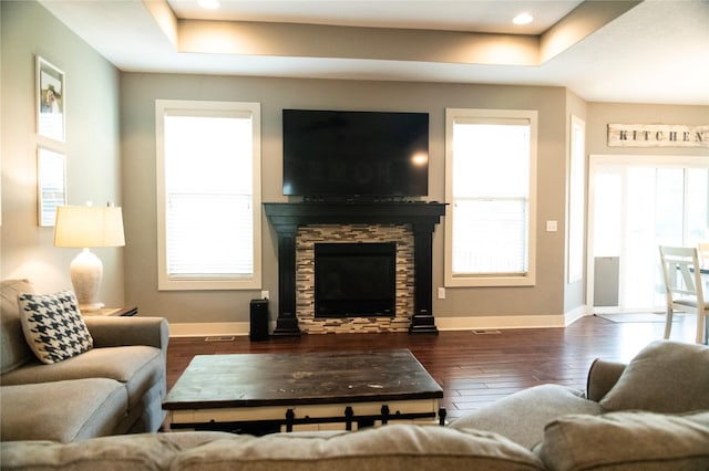 living area featuring a raised ceiling, a fireplace, wood finished floors, baseboards, and recessed lighting