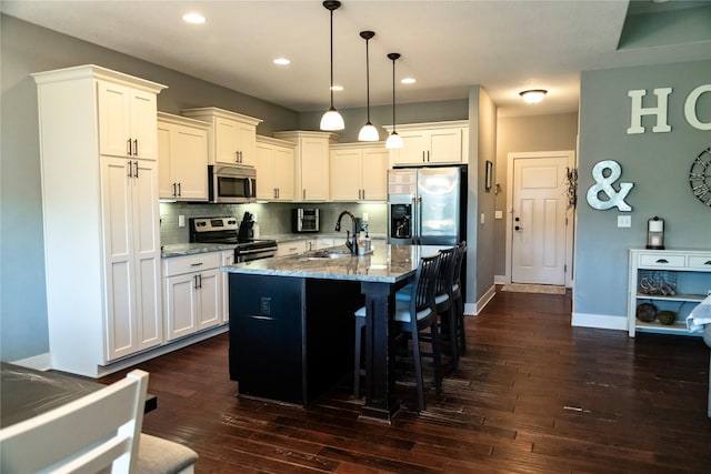 kitchen with appliances with stainless steel finishes, a sink, dark wood finished floors, light stone countertops, and tasteful backsplash