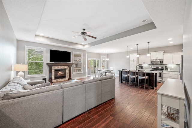235 Emerson Ln, Waukee, IA 50263 - living area featuring a tray ceiling, ceiling fan, dark wood-style flooring, a stone fireplace, and recessed lighting