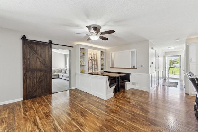 unfurnished living room featuring ceiling fan, a barn door, wood finished floors, baseboards, and a textured ceiling