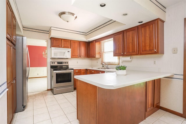 kitchen with appliances with stainless steel finishes, a peninsula, light countertops, brown cabinets, and a sink