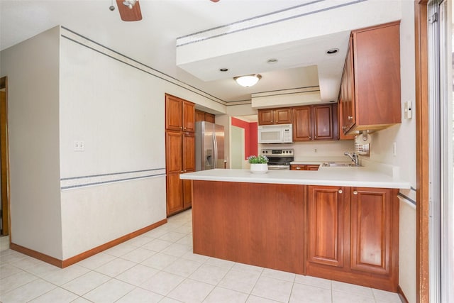 kitchen with appliances with stainless steel finishes, a peninsula, light countertops, a sink, and brown cabinetry