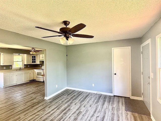 unfurnished living room with dark wood-type flooring, a textured ceiling, ceiling fan, a sink, and baseboards