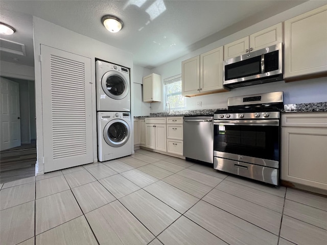 kitchen featuring appliances with stainless steel finishes, stacked washer and clothes dryer, cream cabinets, and light tile patterned flooring