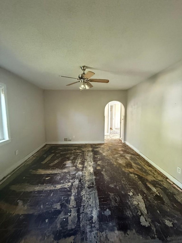spare room featuring arched walkways, a ceiling fan, and baseboards