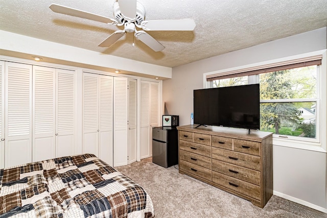 bedroom with freestanding refrigerator, light colored carpet, a textured ceiling, baseboards, and ceiling fan
