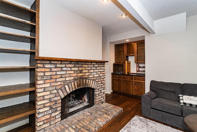 living area with dark wood finished floors, a textured ceiling, and a brick fireplace