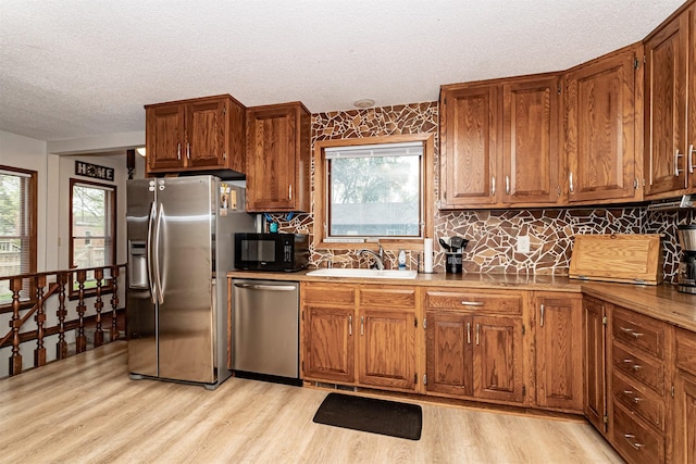 kitchen with appliances with stainless steel finishes, light wood finished floors, a textured ceiling, a sink, and brown cabinets