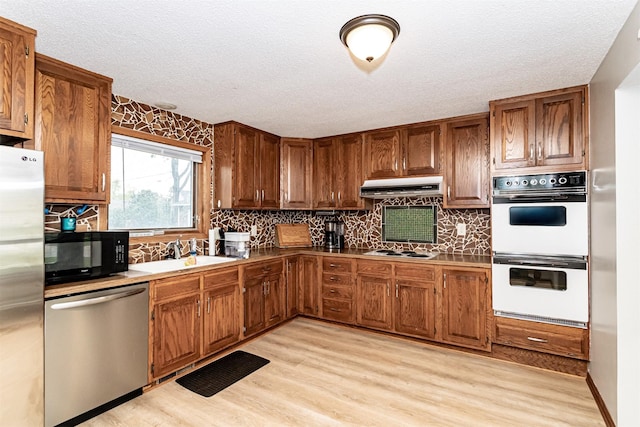 kitchen featuring appliances with stainless steel finishes, a sink, under cabinet range hood, light wood-style floors, and brown cabinets