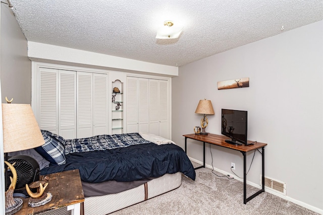bedroom featuring carpet flooring, baseboards, a textured ceiling, and two closets