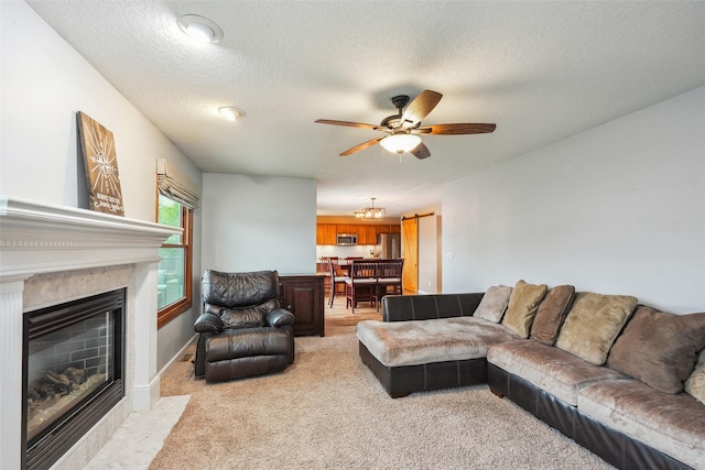 living area with light colored carpet, ceiling fan, a fireplace with flush hearth, and a textured ceiling