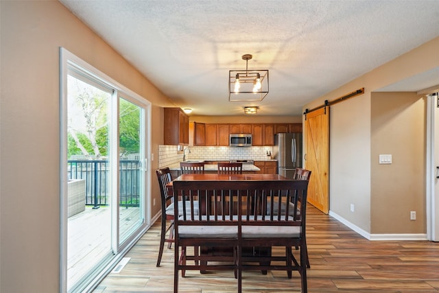 dining room featuring a barn door, light wood-style floors, baseboards, and a textured ceiling