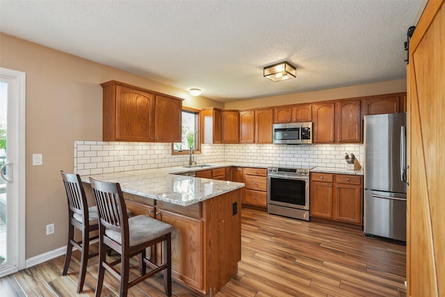 9905 Mcwilliams Dr, Johnston, IA 50131 - kitchen featuring stainless steel appliances, a peninsula, brown cabinetry, tasteful backsplash, and a textured ceiling