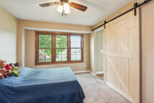 bedroom with a barn door, light carpet, baseboards, and ceiling fan