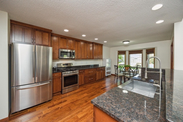 15919 Hawthorn Cir, Clive, IA 50325 - kitchen featuring stainless steel appliances, dark wood-style flooring, a sink, a textured ceiling, and brown cabinets