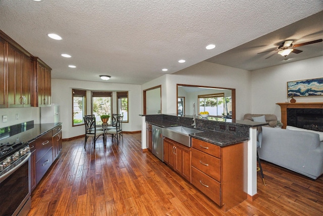 15919 Hawthorn Cir, Clive, IA 50325 - kitchen featuring stainless steel appliances, a sink, dark wood-type flooring, a breakfast bar area, and a glass covered fireplace