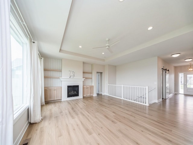 460 NW Gracewood Dr, Waukee, IA 50263 - unfurnished living room with light wood-type flooring, baseboards, ceiling fan, a barn door, and a raised ceiling