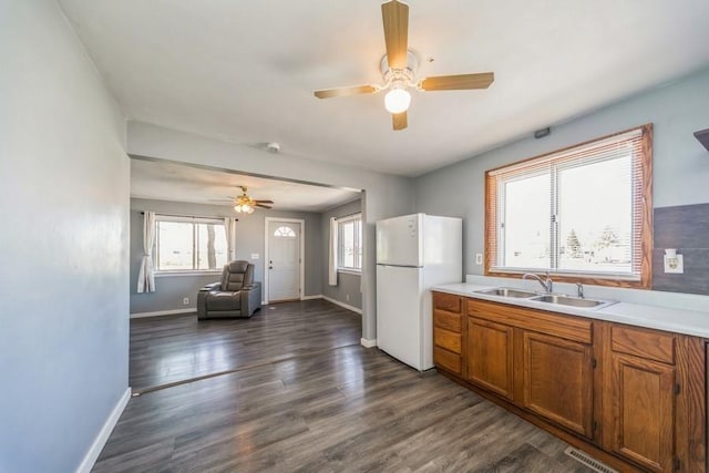 kitchen with a sink, freestanding refrigerator, brown cabinetry, a ceiling fan, and baseboards