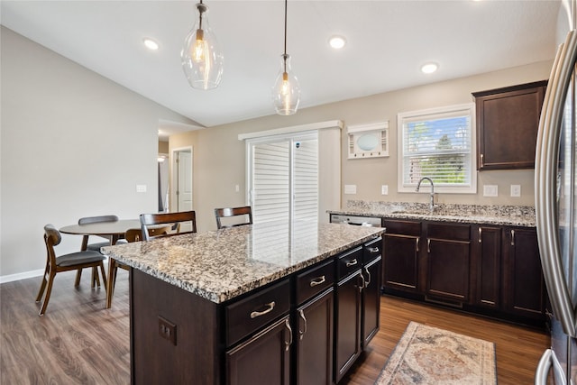 kitchen featuring a sink, freestanding refrigerator, dark wood finished floors, a kitchen island, and decorative light fixtures