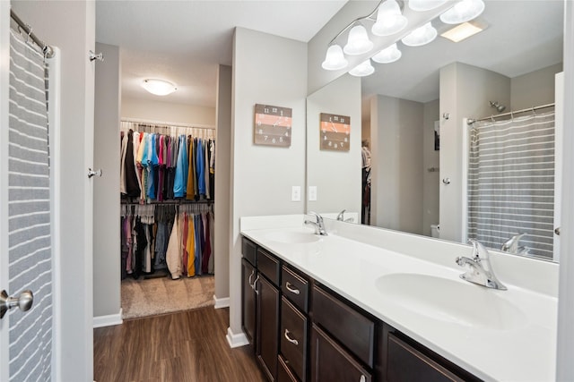 bathroom with wood finished floors, double vanity, a walk in closet, baseboards, and a shower with shower curtain