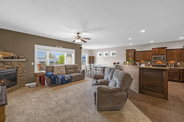 312 Evergreen Dr NW, Bondurant, IA 50035 - tiled living area featuring a ceiling fan, a stone fireplace, recessed lighting, and a sink