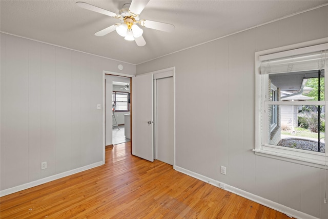 unfurnished bedroom with light wood-style flooring, baseboards, a closet, a ceiling fan, and ornamental molding
