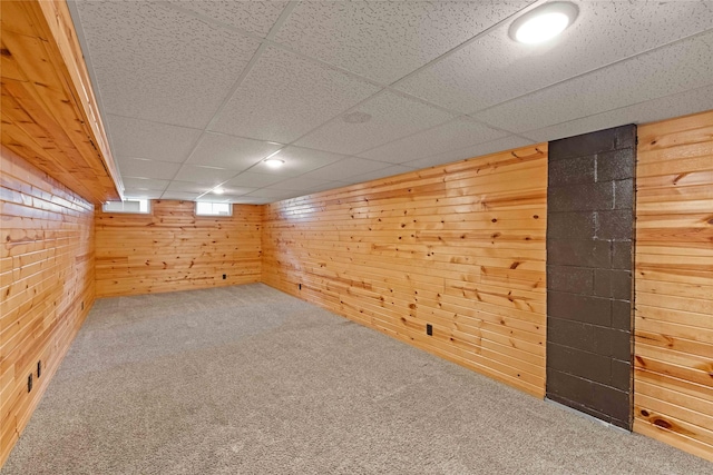 basement featuring wooden walls, carpet, and a paneled ceiling