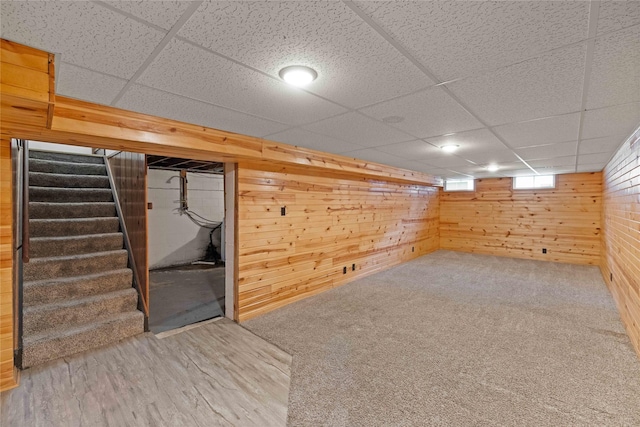 basement featuring a paneled ceiling, wood walls, and stairs