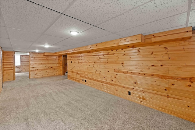 finished below grade area with carpet, wooden walls, and a drop ceiling