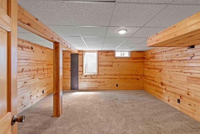below grade area with carpet floors, wood walls, and a drop ceiling