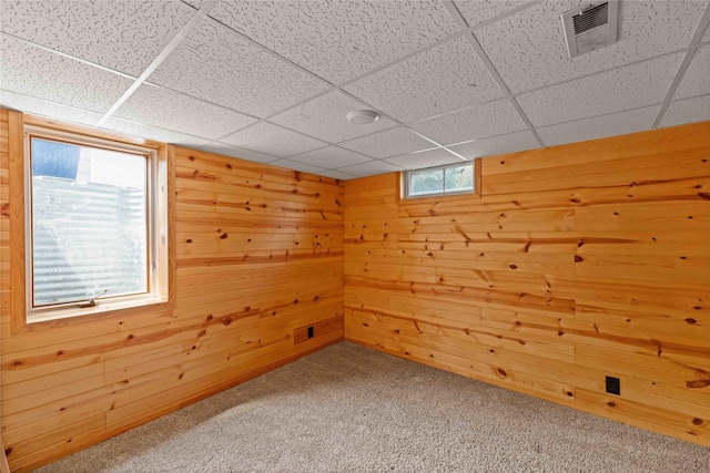 spare room featuring carpet flooring, wooden walls, and a drop ceiling