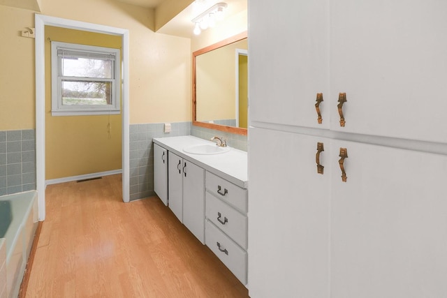 2226 Idaho Dr, Pella, IA 50219 - full bath featuring tile walls, wood finished floors, vanity, a wainscoted wall, and a bathtub