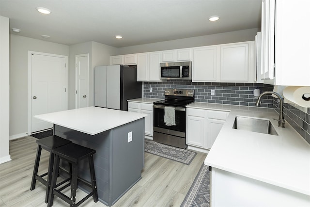 1001 Willow Valley Dr, Norwalk, IA 50211 - kitchen with appliances with stainless steel finishes, a sink, light wood-type flooring, decorative backsplash, and a center island