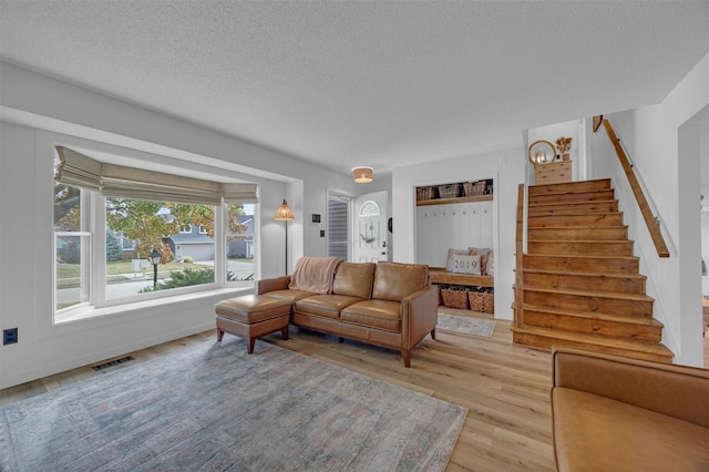 living area featuring light wood-style floors, stairs, a textured ceiling, and baseboards