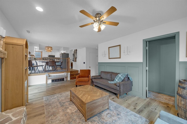 living area with ceiling fan, light wood-type flooring, and a wainscoted wall