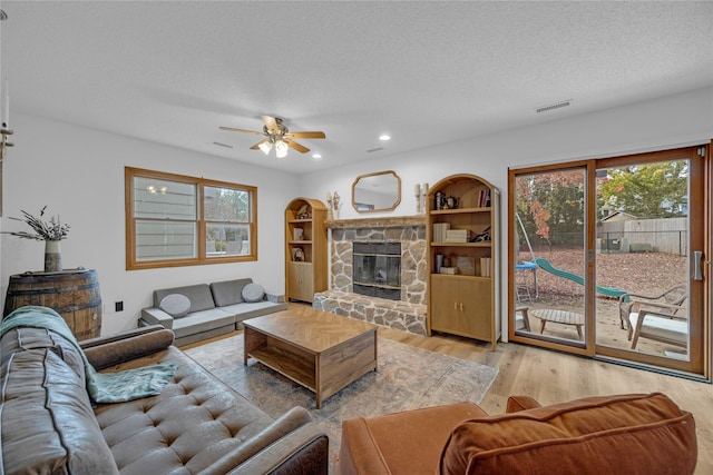 living room featuring wood finished floors, ceiling fan, a textured ceiling, healthy amount of natural light, and a stone fireplace