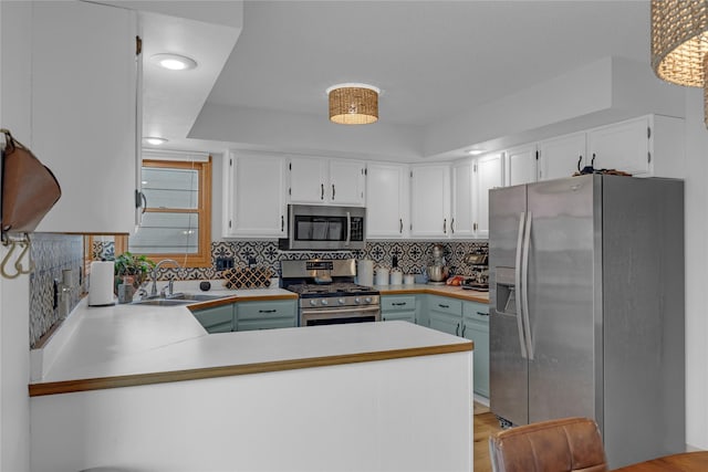 kitchen with stainless steel appliances, a sink, tasteful backsplash, a peninsula, and white cabinetry