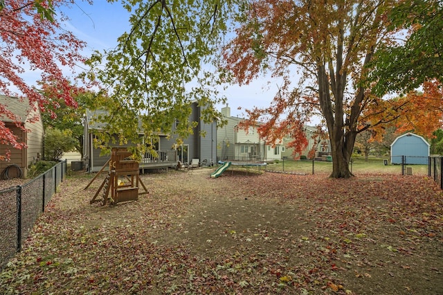 view of yard with a trampoline, fence, a fire pit, and a wooden deck