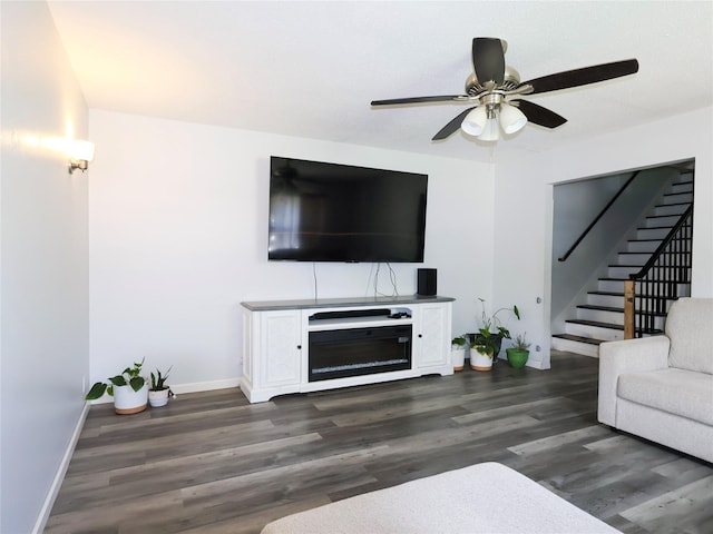 living room featuring stairs, baseboards, dark wood-style flooring, and a ceiling fan