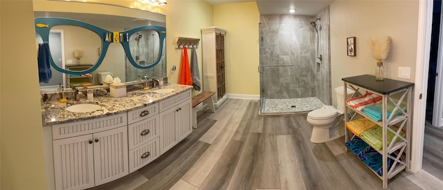 full bath featuring a stall shower, wood finished floors, double vanity, toilet, and baseboards