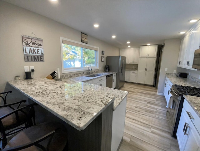 kitchen with stainless steel appliances, a sink, a peninsula, white cabinets, and recessed lighting