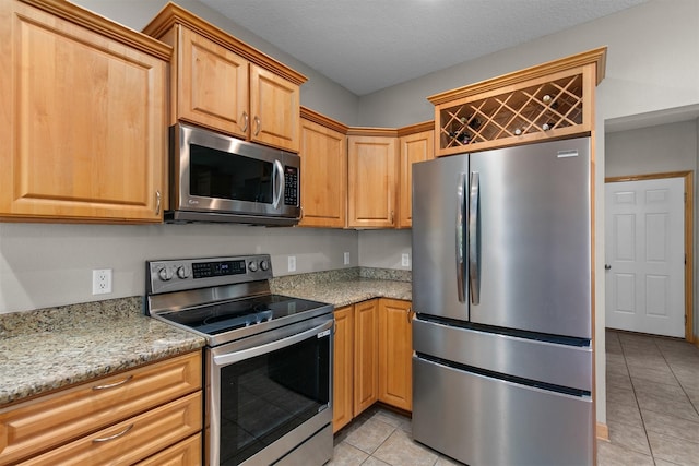 kitchen featuring stainless steel appliances, light tile patterned floors, and light stone counters