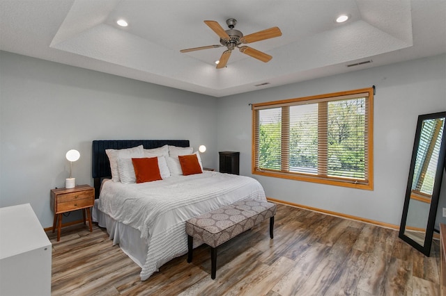 bedroom with a tray ceiling, wood finished floors, baseboards, recessed lighting, and ceiling fan
