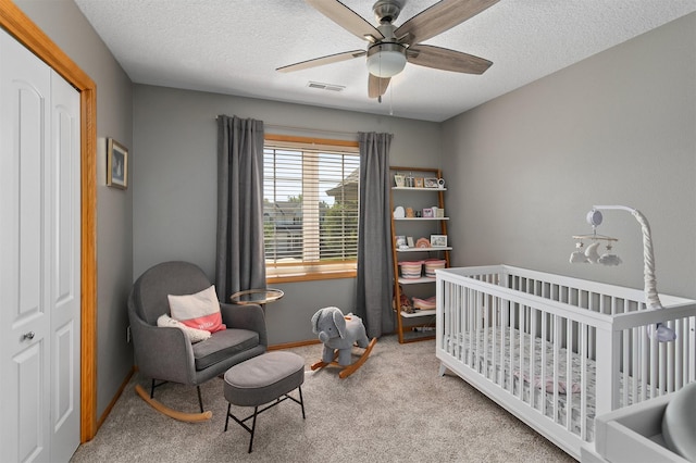 bedroom with carpet flooring, a crib, a textured ceiling, ceiling fan, and baseboards