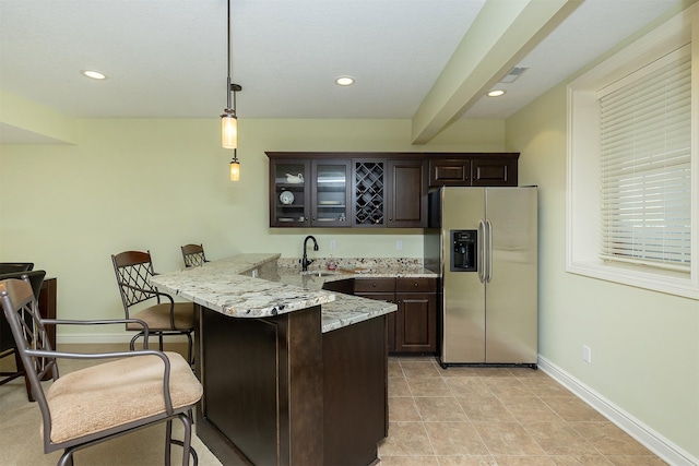 1914 Park Ave, Des Moines, IA 50315 - kitchen featuring stainless steel fridge with ice dispenser, a peninsula, a breakfast bar area, dark brown cabinetry, and glass insert cabinets