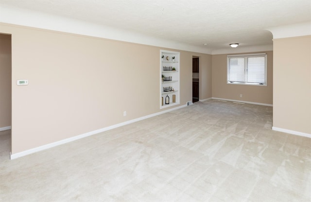 unfurnished room with built in features, light carpet, and baseboards