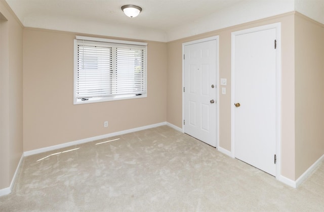 spare room featuring light carpet and baseboards