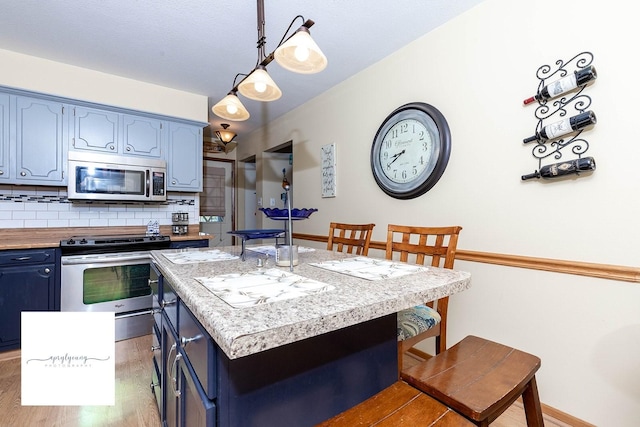 6404 Meredith Dr, Urbandale, IA 50322 - kitchen featuring appliances with stainless steel finishes, blue cabinets, a breakfast bar area, light wood-type flooring, and decorative backsplash