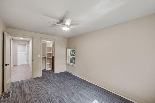 504 9th St, West Des Moines, IA 50265 - unfurnished bedroom with baseboards, a closet, a ceiling fan, dark colored carpet, and a walk in closet